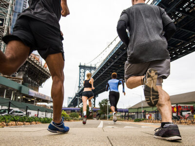 2021 NYC Marathon - The image shows people running through New York City streets from a view under a bridge.